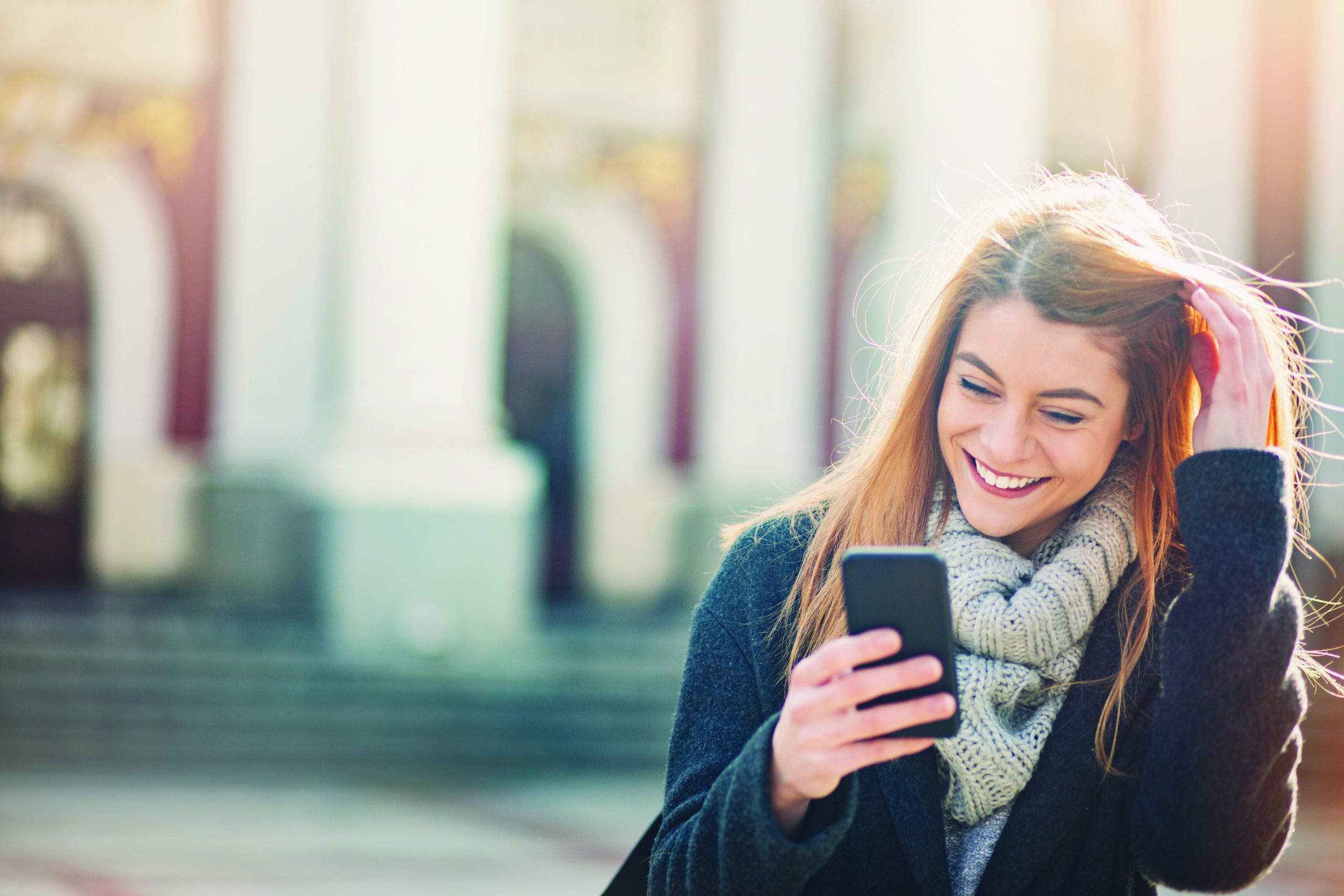 Young smiling woman checking her phone at city setting, with copy space